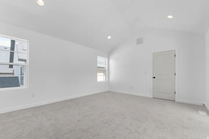 Spacious room featuring vaulted ceilings, recessed lighting, two windows, neutral carpet flooring, and a flat-panel interior door with matte black hardware