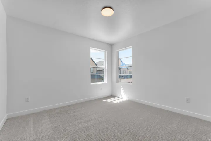 Neutral-toned room featuring a light-colored carpet, white walls, and two multi-pane windows