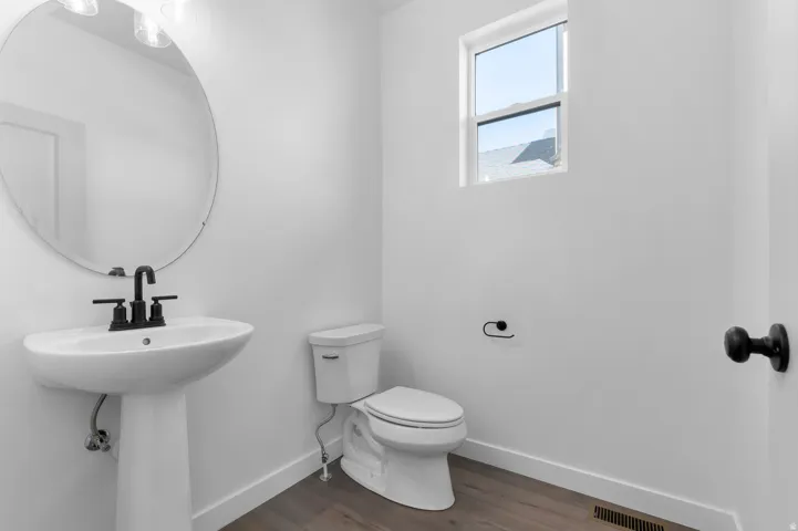 Powder room featuring a pedestal sink with matte black hardware, a round mirror, and wood-finish flooring