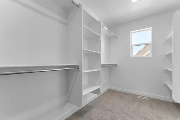 Spacious walk-in closet featuring white built-in shelving, chrome hanging rods, recessed lighting, and a window for natural illumination