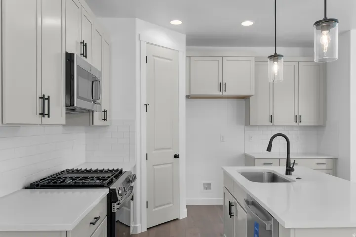 Kitchen featuring white shaker-style cabinetry with black hardware, white subway tile backsplash, stainless steel appliances, and a kitchen island with an undermount sink and black faucet
