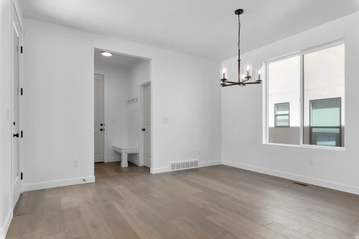 Spacious interior room with wood-finish flooring, a large window, and a contemporary black chandelier