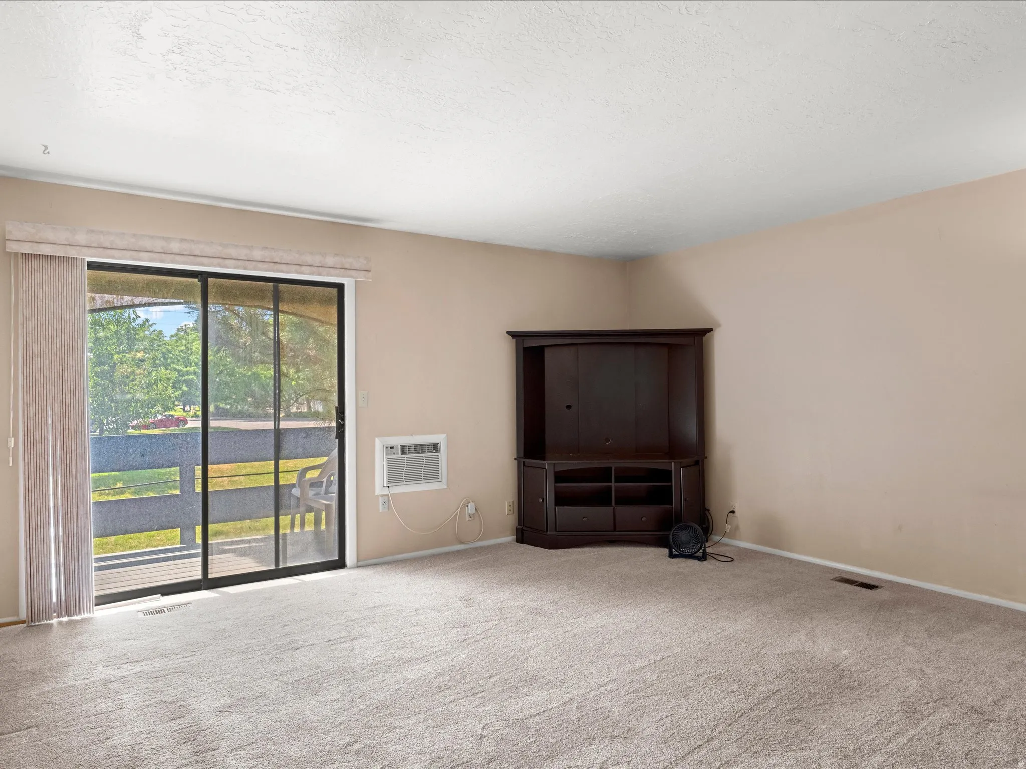 Carpeted living area featuring a large sliding glass door, a window-mounted air conditioning unit, and neutral-toned walls