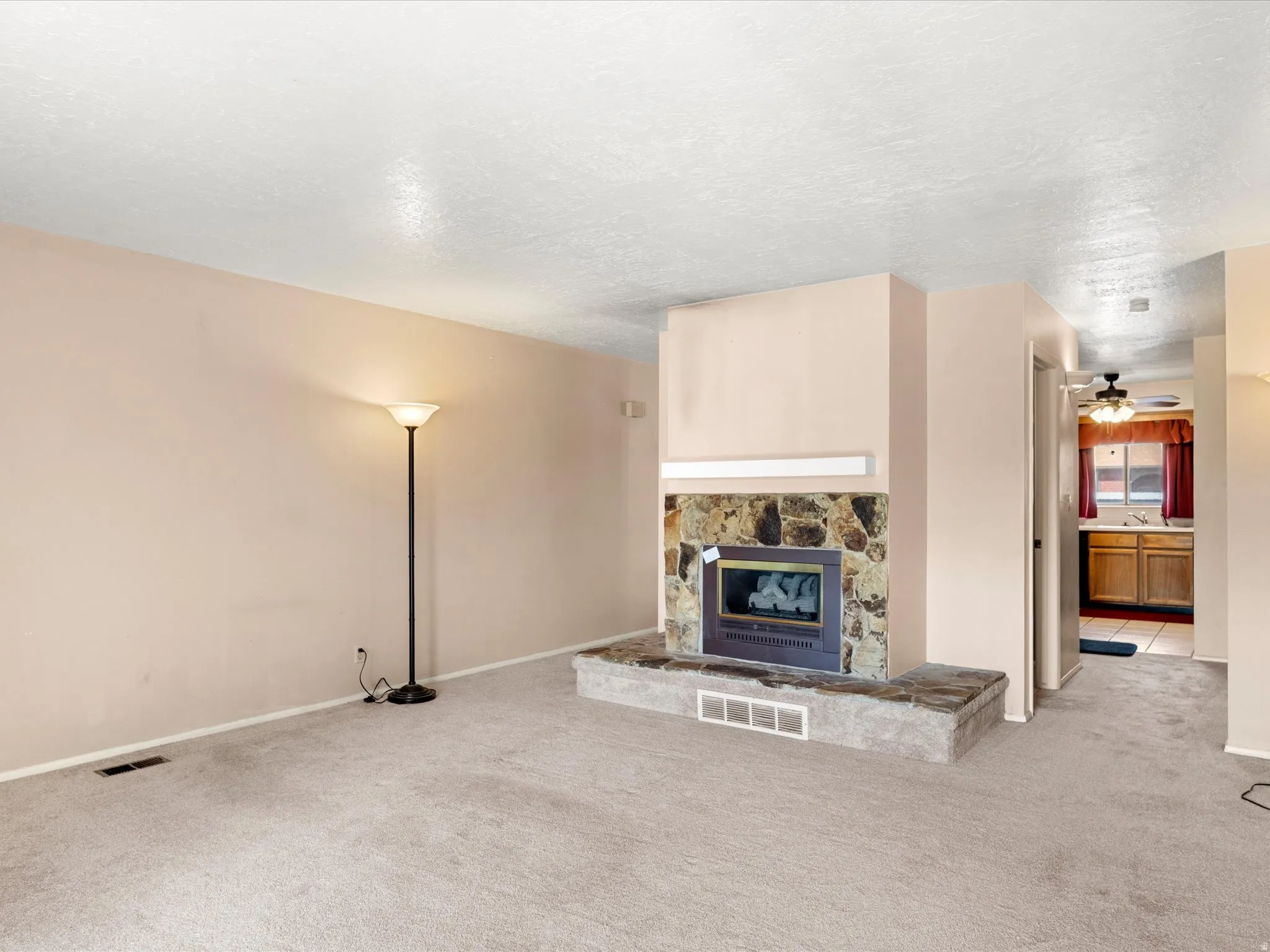 Living area featuring a stone-clad fireplace with a raised hearth, light-toned carpeting, and neutral wall paint