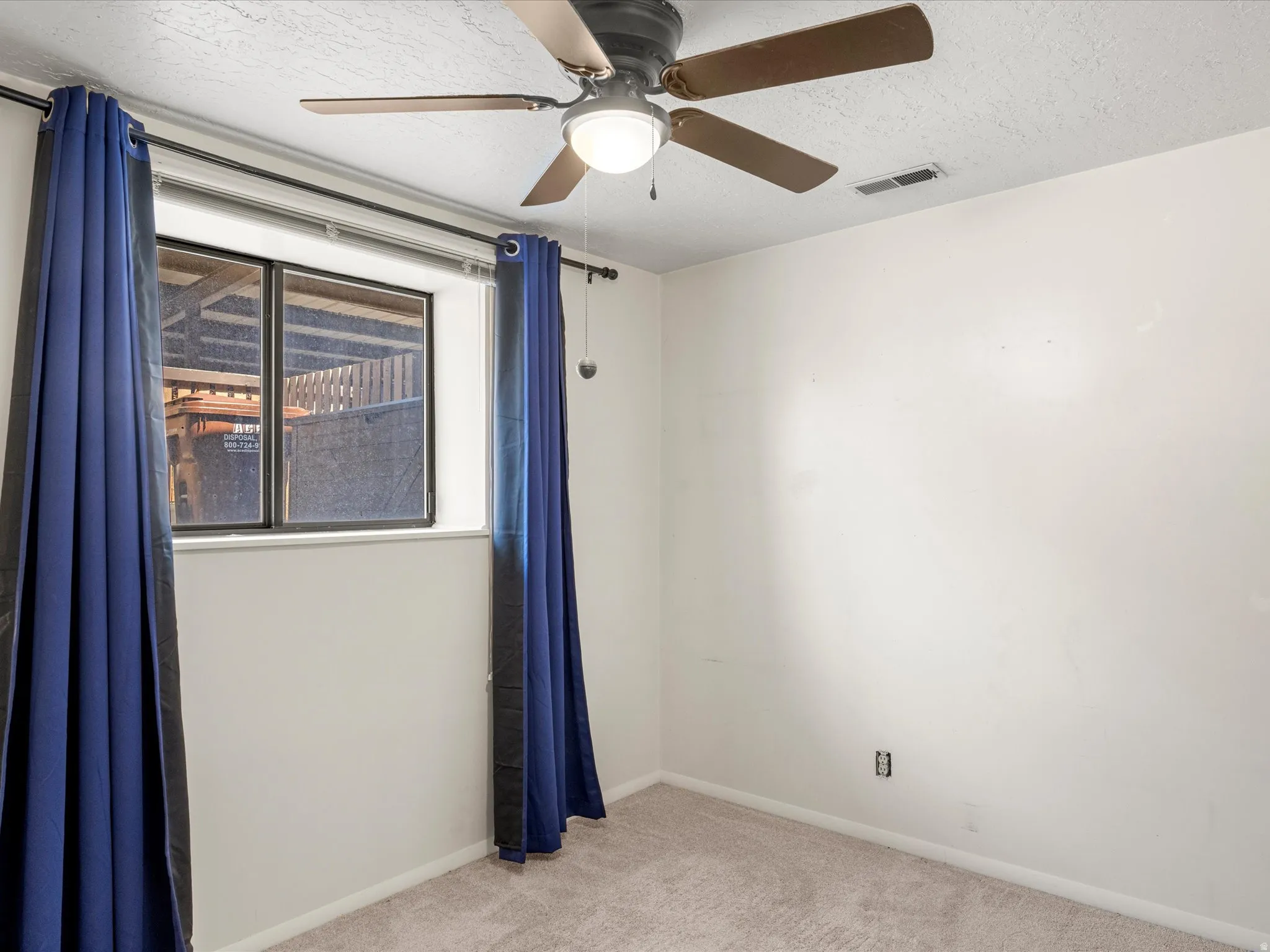 Neutral wall color with textured ceiling, ceiling fan with light fixture, window, and carpeted flooring