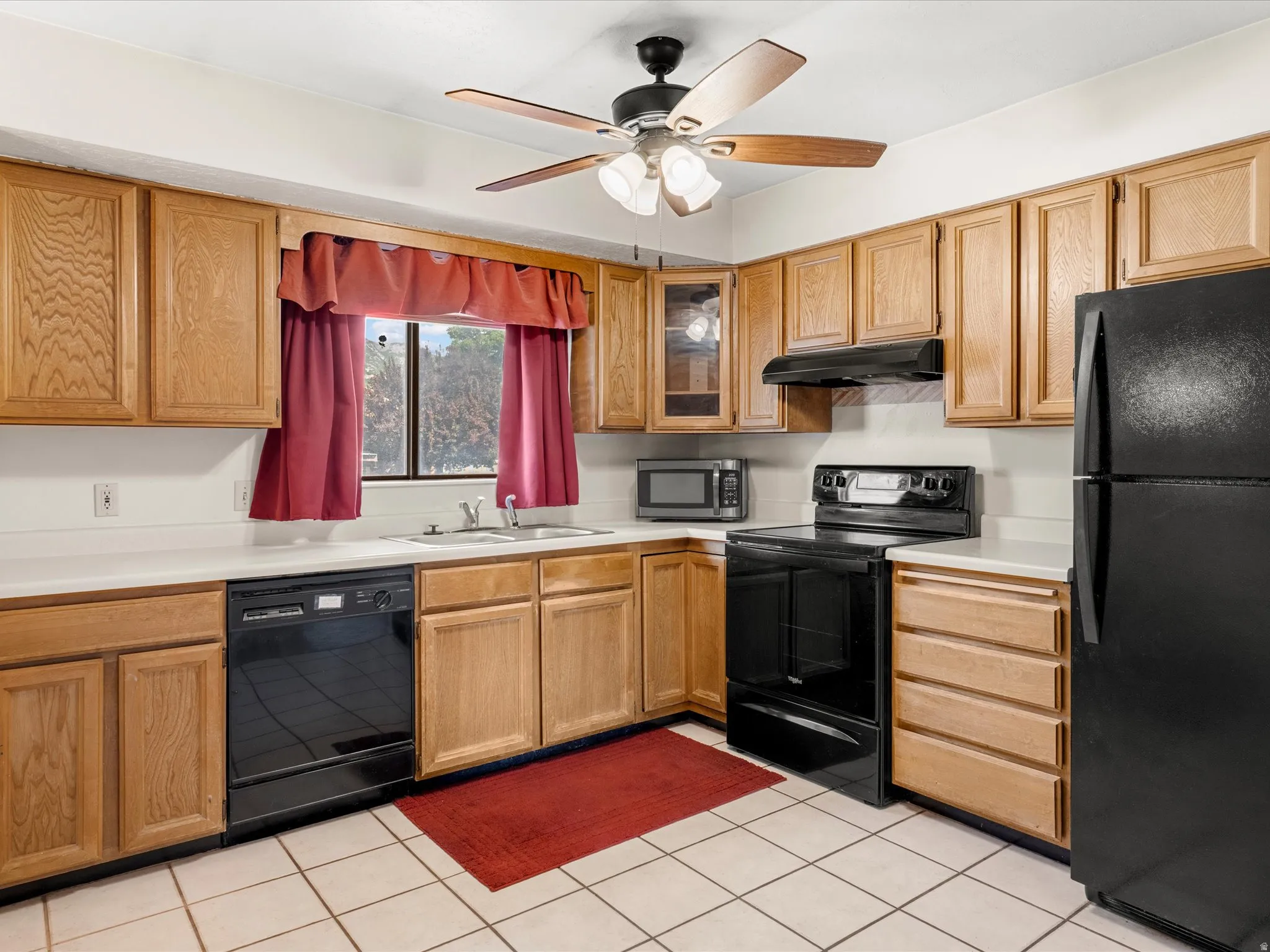 Kitchen featuring wood cabinetry, white countertops, tile flooring, and black appliances including a refrigerator, range, and dishwasher