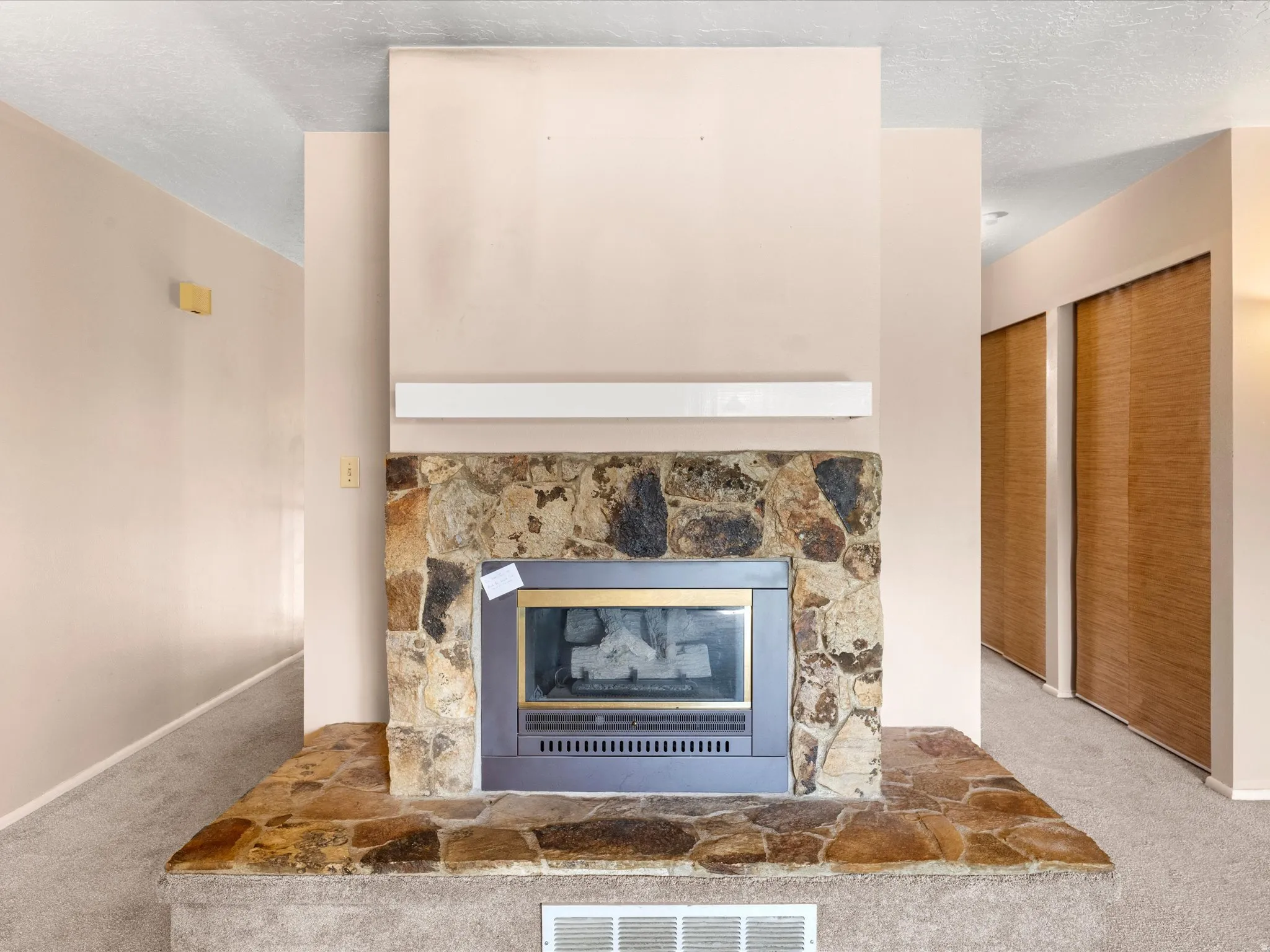 Stone-clad fireplace with a metal insert, a raised stone hearth, and a mantel shelf