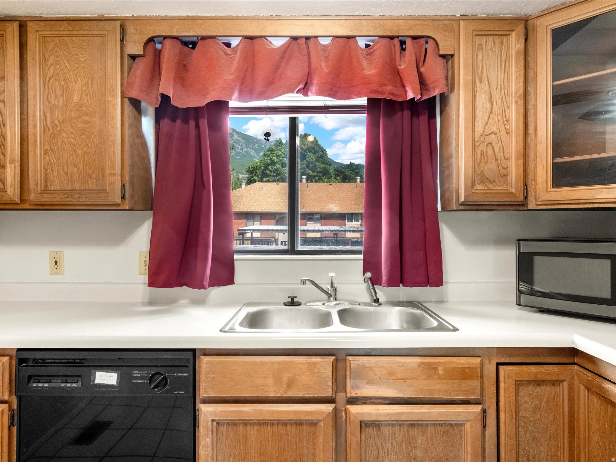 Kitchen featuring wood-finish cabinetry, white countertops, a double basin stainless steel sink, and a built-in dishwasher