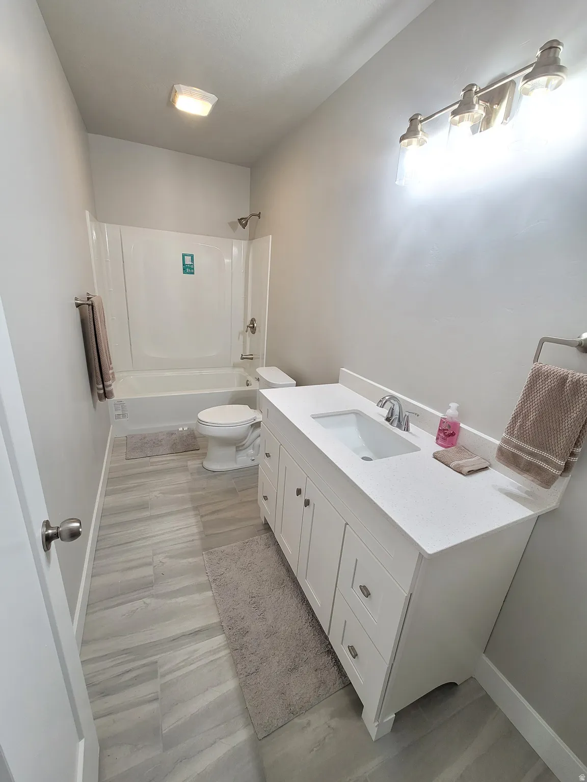 Full bathroom featuring a white vanity with an integrated sink, quartz-finish countertop, and brushed nickel hardware