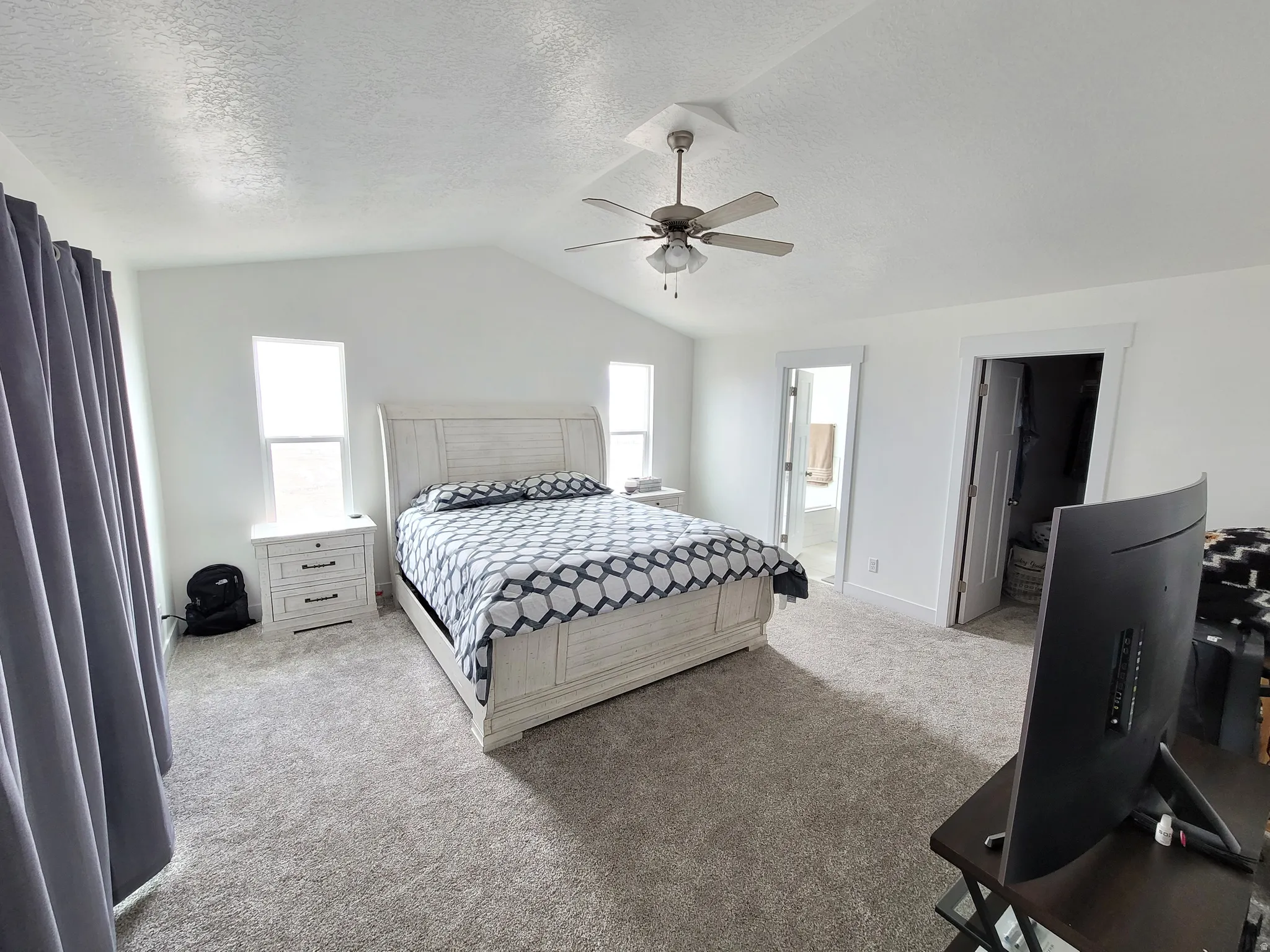 Expansive room featuring vaulted ceilings, a ceiling fan with integrated lighting, and neutral-toned carpeting