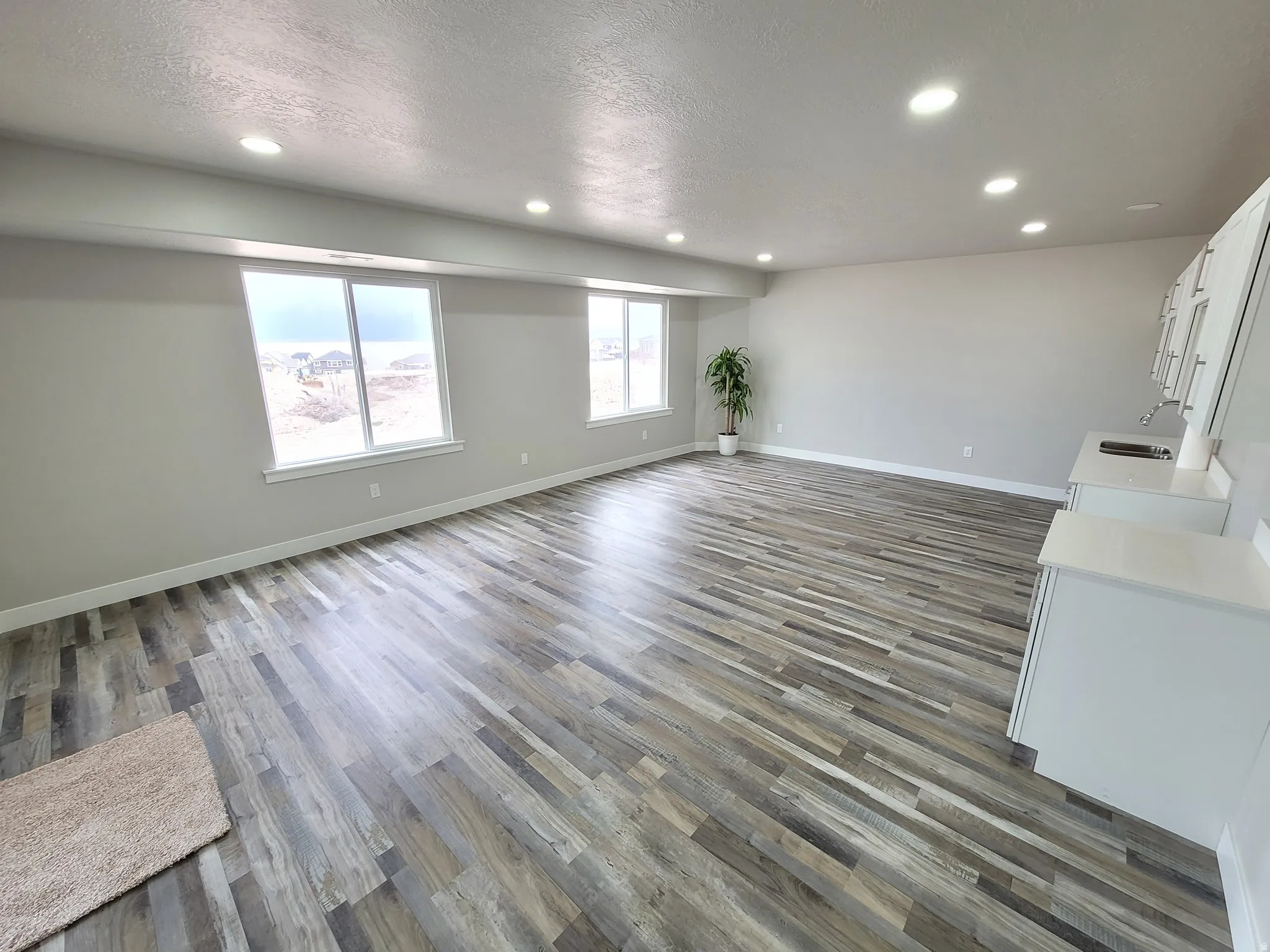 Spacious room featuring wood-finish flooring, two large windows, recessed lighting, and a built-in wet bar with white cabinetry and a countertop