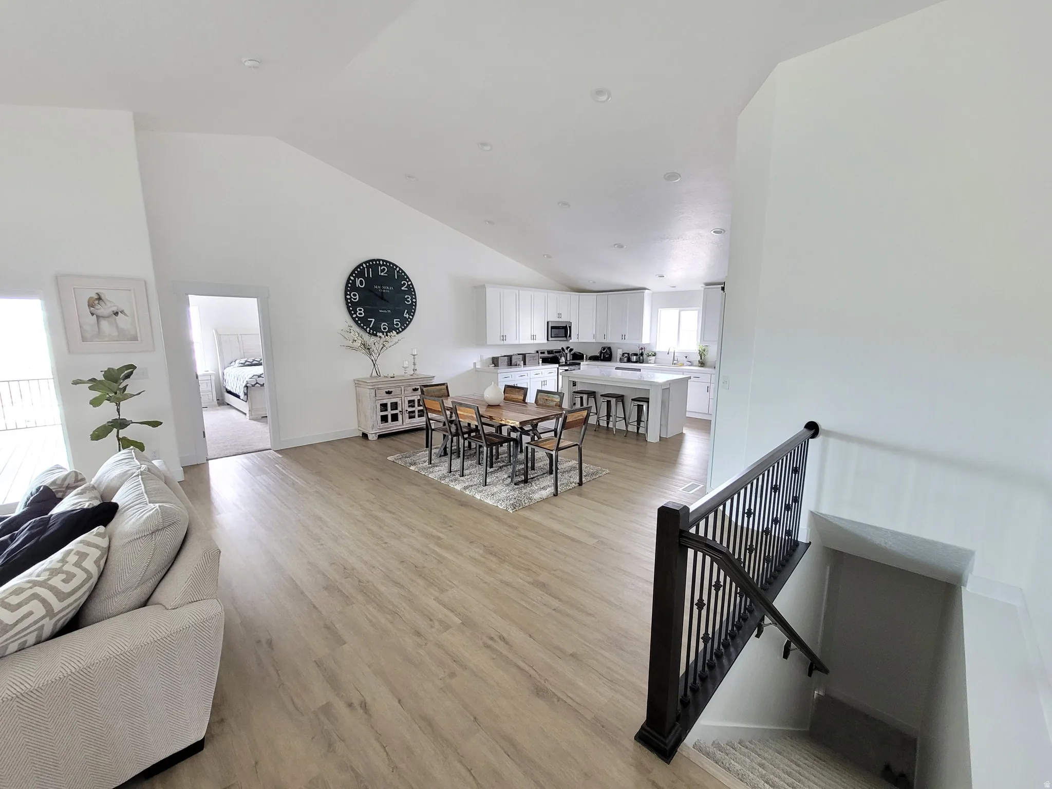 Open-concept living space featuring vaulted ceilings, wood-finish flooring, a contemporary kitchen with white cabinetry and an island, and a dining area with a modern light fixture