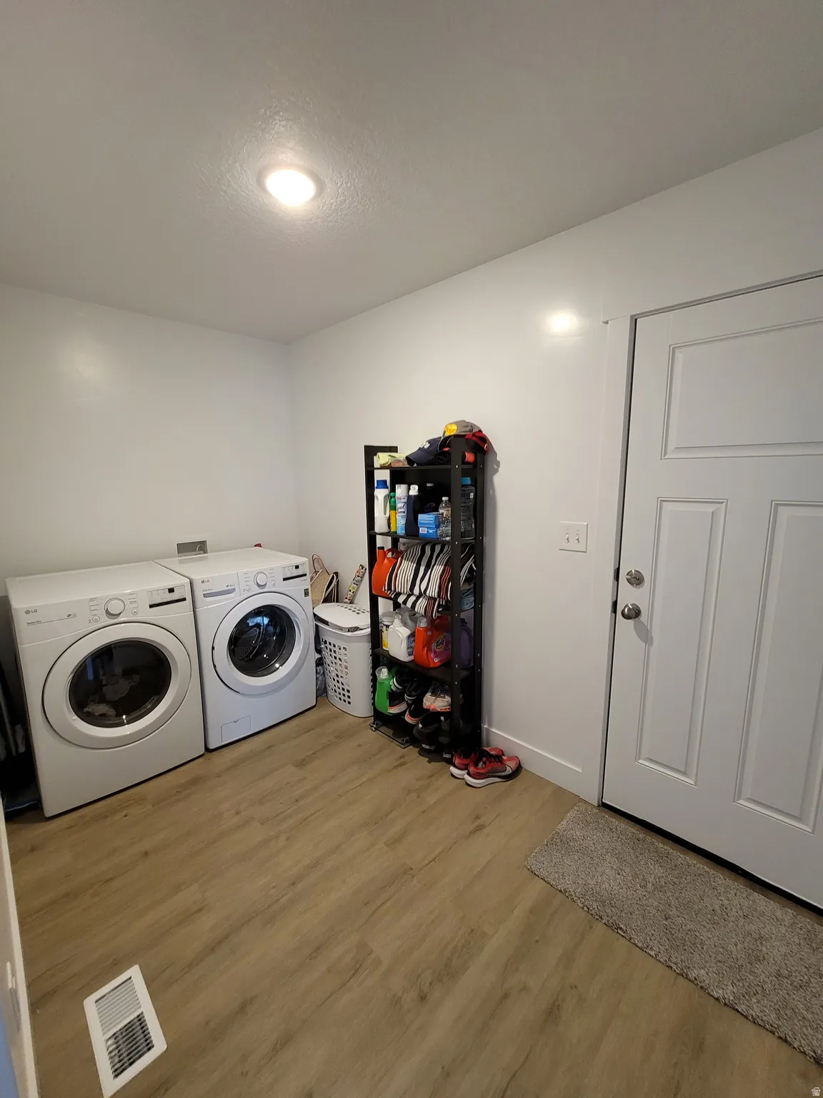 Dedicated laundry area featuring wood-finish flooring, light neutral wall paint, and overhead lighting