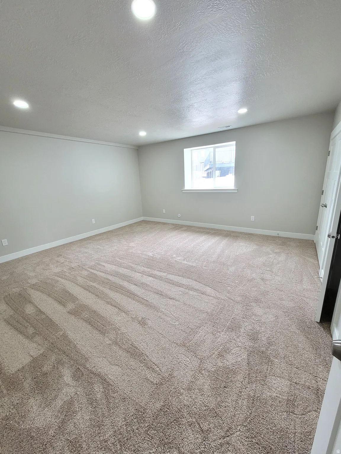 Spacious room featuring neutral carpeting, recessed lighting, a single window, and light-toned wall paint