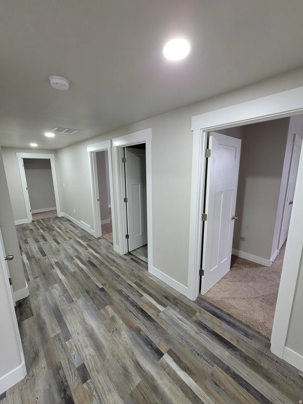 Hallway featuring wood-finish flooring, recessed lighting, white trim, and neutral wall tones