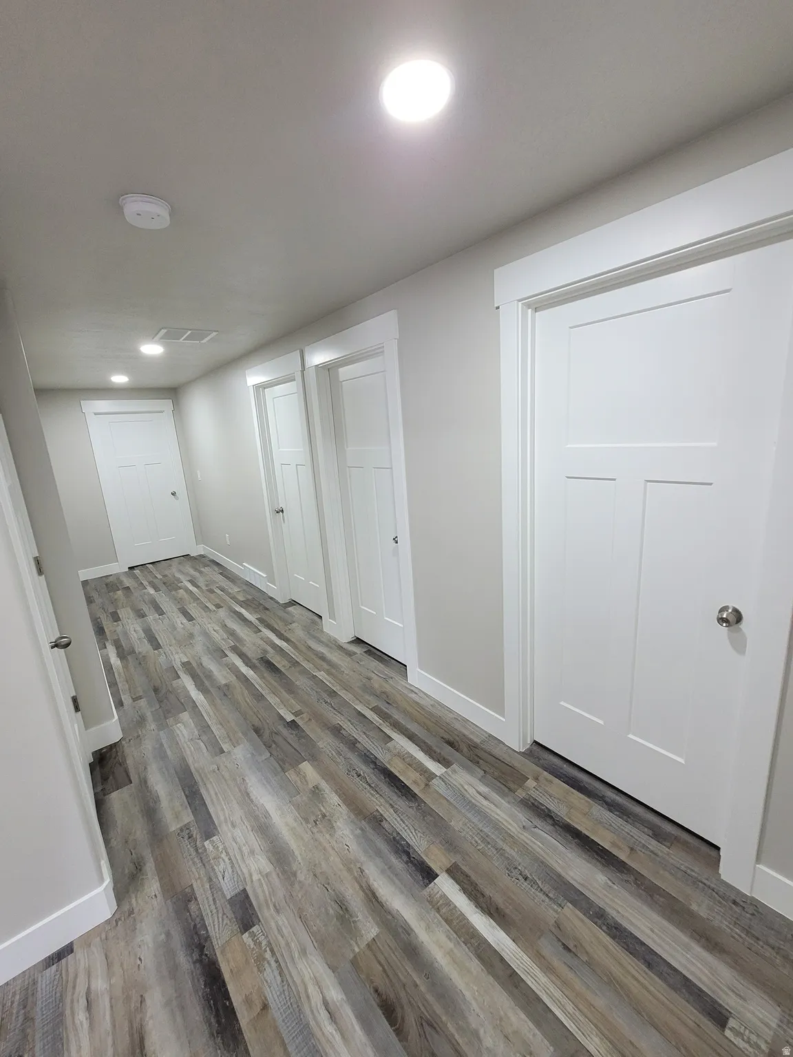 Hallway featuring wood-finish flooring, recessed lighting, white doors with panel detailing, and coordinating white trim