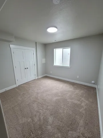Spacious room featuring neutral carpeting, light gray walls, a white trim window, a flush-mount ceiling light, and white double-panel doors