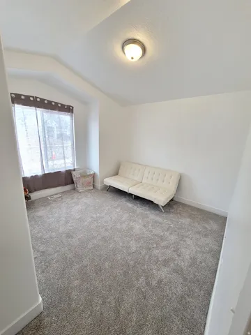 Carpeted room featuring a ceiling-mounted light fixture, a window with curtain rods, and white baseboards