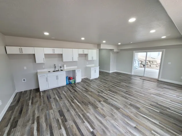 Spacious open room featuring wood-finish flooring, recessed lighting, and a full wall of white cabinetry with a sink