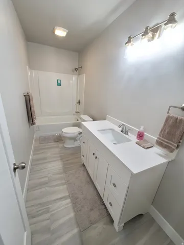 Full bathroom featuring a white vanity with an integrated sink, quartz-finish countertop, and brushed nickel hardware