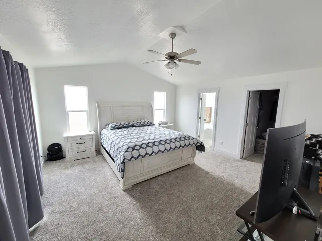 Expansive room featuring vaulted ceilings, a ceiling fan with integrated lighting, and neutral-toned carpeting
