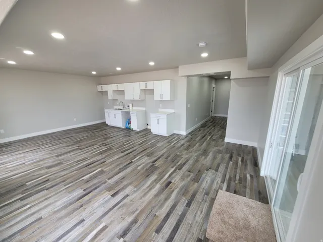 Open concept living space featuring wood-finish flooring, recessed lighting, and a built-in kitchenette with white cabinetry and a stainless steel sink