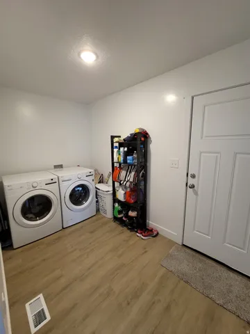 Dedicated laundry area featuring wood-finish flooring, light neutral wall paint, and overhead lighting