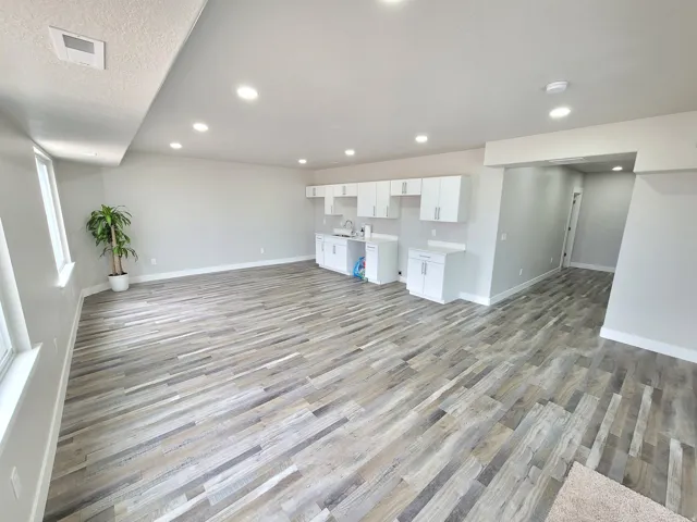 Open-concept area featuring wood-finish flooring, recessed lighting, and a built-in kitchenette with white cabinetry and a stainless steel sink