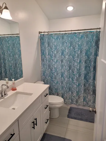 Bathroom featuring a white vanity with an integrated sink and matte black hardware, a toilet, and large format tile flooring