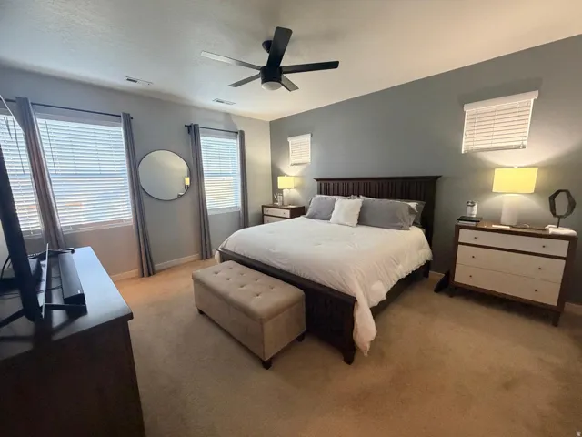 Carpeted bedroom featuring a ceiling fan, multiple windows with blinds, a large bed frame, and a dresser