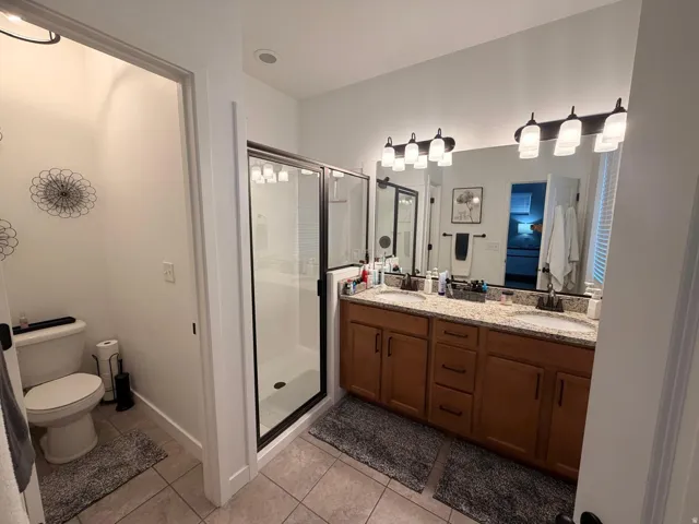 Bathroom featuring a dual vanity with a granite-style countertop, wood-finish cabinetry, and individual rectangular sinks
