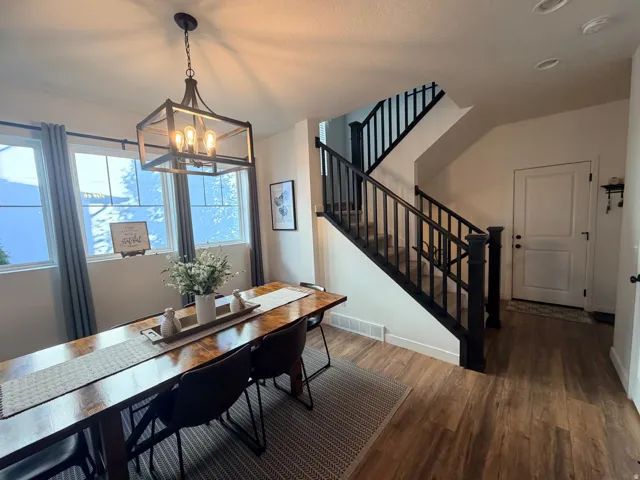 Open-concept dining area featuring wood-finish flooring, a contemporary chandelier, multiple windows, and a staircase with dark wood railings