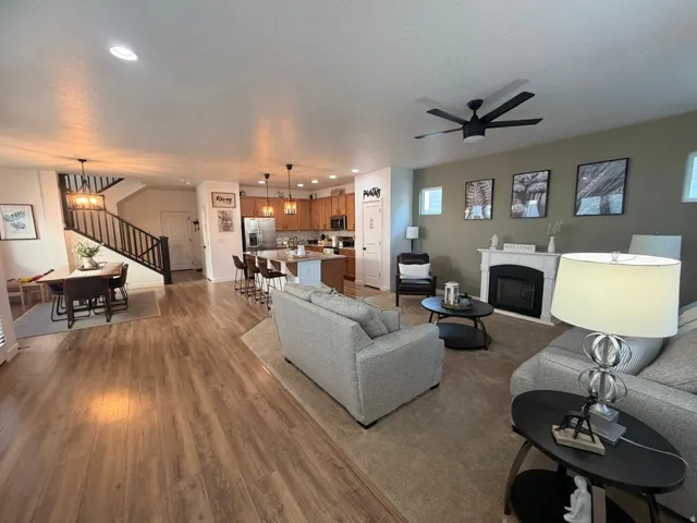 Open-concept living area with wood-finish flooring, a contemporary fireplace with a white mantel, and a multi-blade ceiling fan