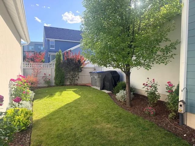 Manicured lawn area featuring a mature tree, a variety of colorful shrubs, and flowering plants