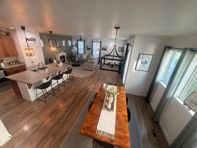 Open-concept main level featuring wood-finish flooring, a kitchen island with stone countertop, pendant lighting, and a fireplace with mantle