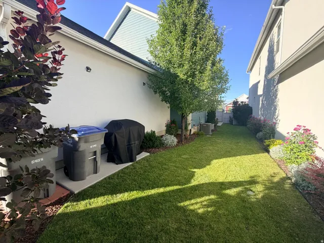 Side yard featuring a manicured lawn, established landscaping, and mature trees