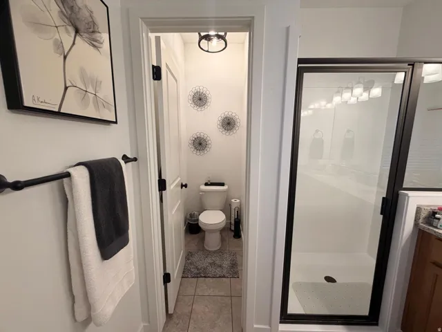 Walk-in shower with black-framed glass enclosure, tiled flooring, and modern overhead lighting