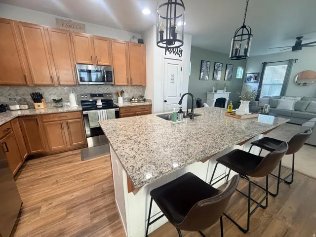 Kitchen featuring an expansive island with a built-in sink, granite countertops, wood-finish flooring, stainless steel appliances, and natural wood cabinetry