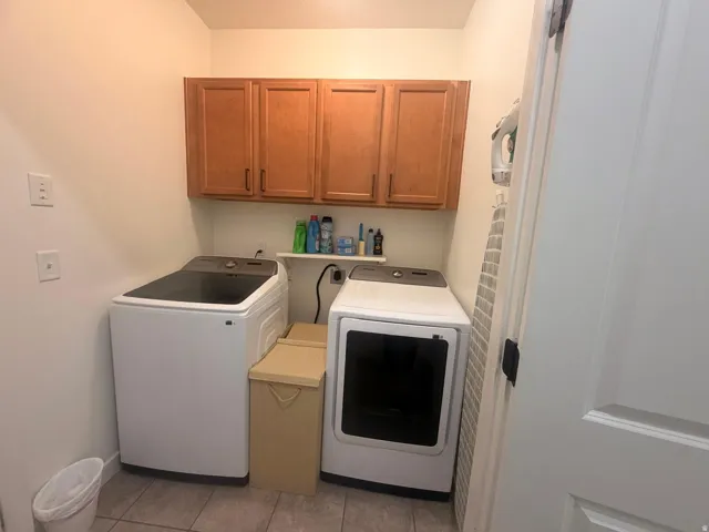 Functional laundry area featuring upper wood-finish cabinetry, a white wall-mounted shelf, and neutral-toned tile flooring