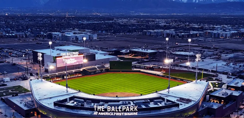 Aerial panorama showcasing a modern ballpark with illuminated green turf and surrounding urban development