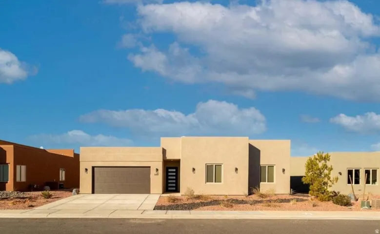 Stucco exterior with a flat roofline, two-car garage, contemporary entry door with vertical frosted glass panels, and desert-style landscaping