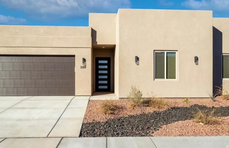 Contemporary stucco exterior with a flat roofline, integrated garage, concrete driveway, and minimalist landscaping