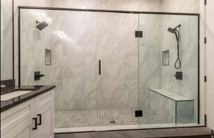 Spacious shower enclosure with dual showerheads, integrated bench seating, and dark-framed glass doors