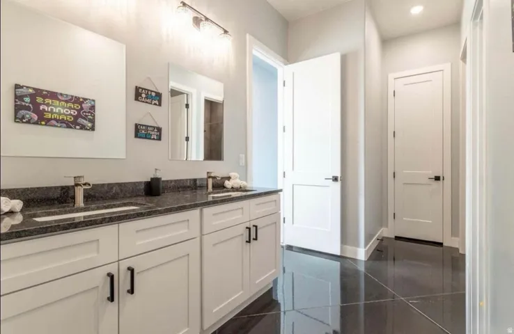 Dual vanity with undermount sinks, dark granite countertop, white shaker-style cabinetry, and dark tile flooring