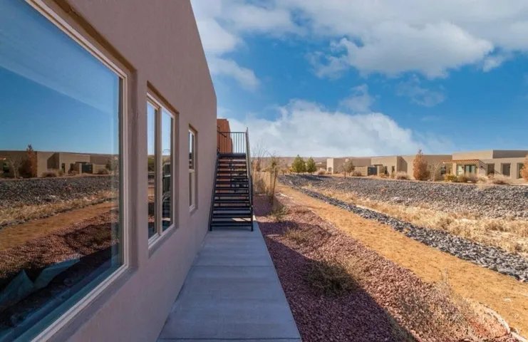 Stucco exterior with multiple windows, concrete walkway, and exterior metal staircase