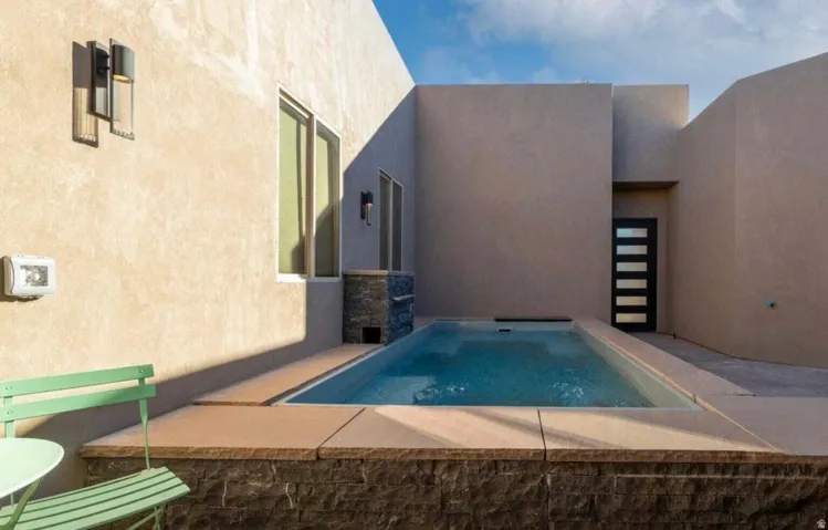 Private outdoor area featuring a rectangular pool, stucco exterior walls, stone veneer detailing, and a multi-paneled dark entry door
