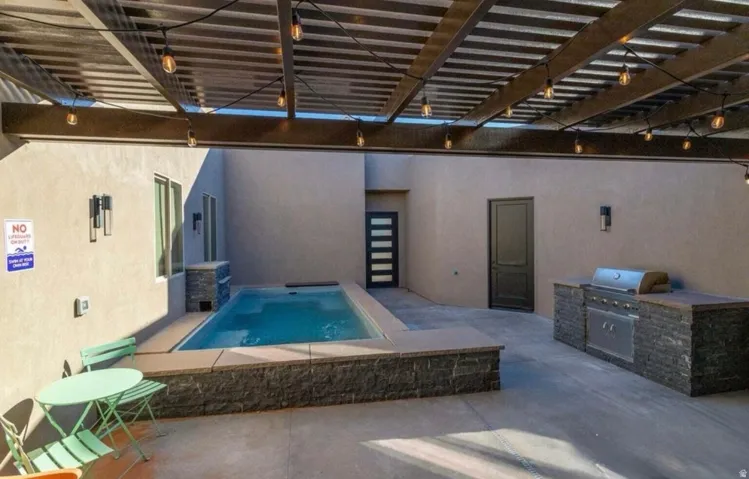 Private courtyard featuring a plunge pool, built-in outdoor kitchen with grill, a slatted pergola, and string lighting