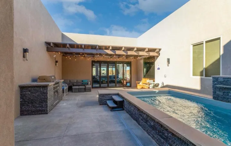 Private courtyard featuring a plunge pool, built-in outdoor kitchen with stone veneer, and a covered patio with a wood pergola