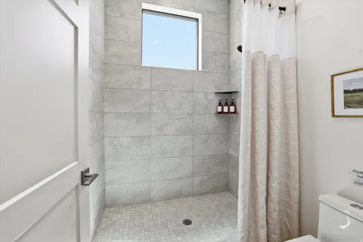 Walk-in shower featuring large format gray wall tiling and mosaic floor tiles