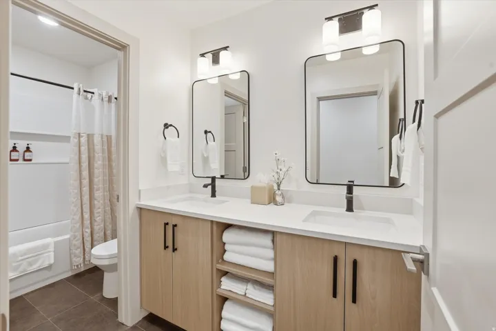 Bathroom featuring a dual vanity with light wood-finish cabinetry, white countertops, and black hardware